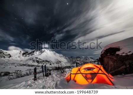 Orange tent on snow in mountains at night
