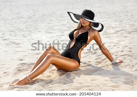 Sexy woman in a swimsuit sitting on the sand of the beach. Tan skin
