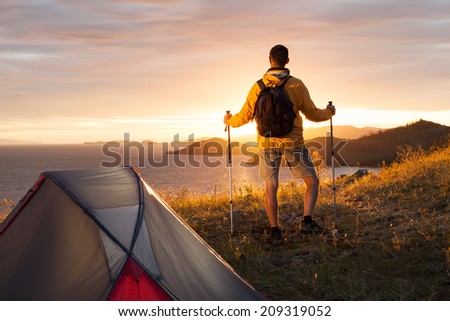 Man looking at beautiful sunrise at big lake near tent
