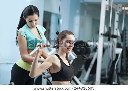 Woman at the health club with her personal trainer, learning the correct form on the pull-down machine.