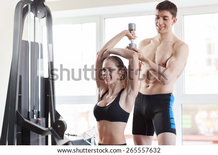 Woman at the health club with her personal trainer, learning the correct form with barbell