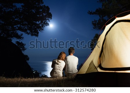 Silhouette of couple near tent looking at moon at night