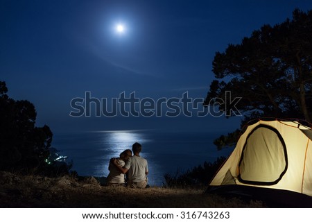 Couple close to tent looking at moon night above sea