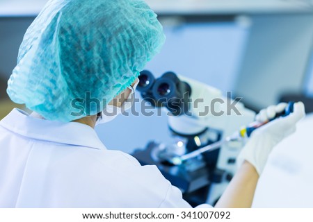 Rear view of Scientist holding pipette working a microscope at the laboratory
