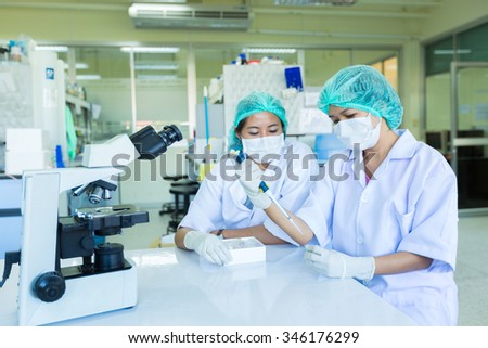 Scientists with pipette and test tube, examining samples and liquid in laboratory