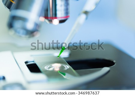 Scientist dropping chemical liquid on the slide at microscope,