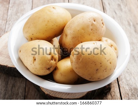 raw potatoes in white plate on wooden background