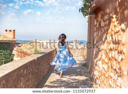 France, Provence medieval town Roussillon. Pretty young woman  in blue dress walking down the street in Provencal old city.  Travel and wanderlust concept. June - time of blooming lavender in Provence