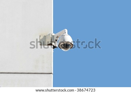 surveillance camera at a white wall with blue sky background
