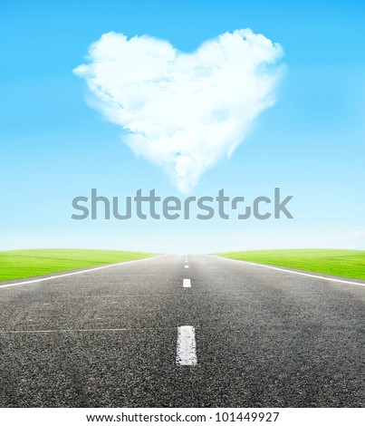 green field and road over blue sky with clouds in shape of  heart - honeymoon travel concept