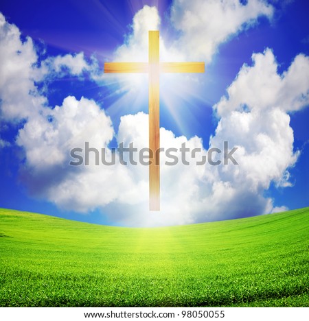 shiny wooden easter cross over green field and blue sky with sun rays