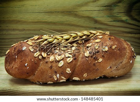Traditional bread with seeds of oat and ear on wood background