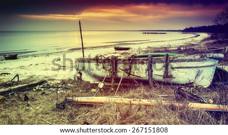 Anchored old fishing boat on sandy beach of the Baltic Sea. Image toned in vintage warm colors style
