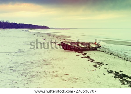 Anchored fishing boat on sandy beach of the Baltic Sea. Image toned in vintage warm colors style