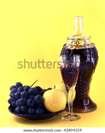 old bottle and glass with wine against fruits on yellow background