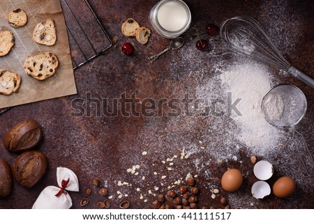 Bakery background, baking ingredients over rustic kitchen countertop. Baked cookies with hazelnuts, rye bread, milk and eggs. Top view, copy space.