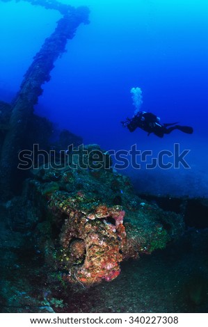 Scuba diver underwater photographer swimming over WWII tank on the deck of ship wreck   full sea anemones and corals.30 meters depth. Truk Lagoon.Micronesia.