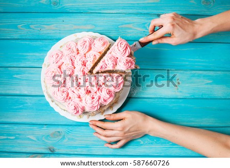 Woman\'s hands cut the cake with pink cream on blue wood background. Pink cake. Top view