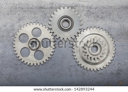 Three steel gears interlocked on a dirty steel background.