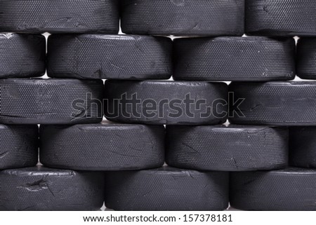 A close up photo of a wall of well used hockey pucks.