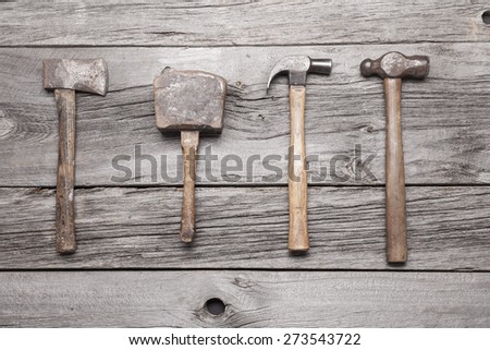 A vintage hatchet, mallet, claw hammer and ball-peen hammer sit on a rustic wooden background.