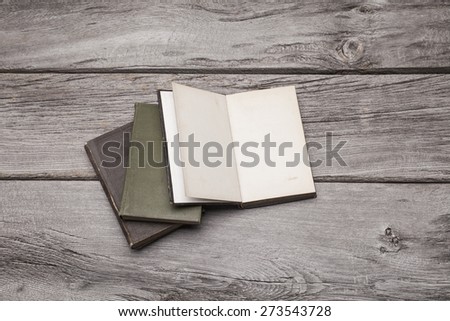 A pile of blank antique books sit on a rustic wooden background. The top book on the pile is open and can be used to display your content.