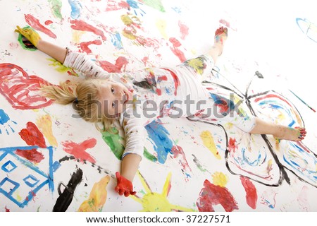 Closeup of a smiling child full of paint and laying on a painted floor