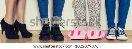 Female legs in cute pink monster foot slippers with big claws and other in different kind of shoes. Be original concept. Standing out of the croud - individuality.