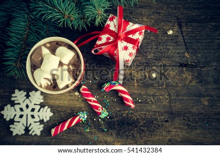 Cup of winter hot drink cacao with marshmallows and candy on old wooden table. Spicy hot chocolate with fir tree, snowflake and present. Happy New Year. Moody style. Top view. Copy space.