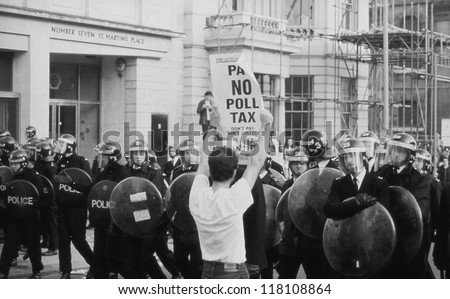LONDON - MARCH 31: A protestor holds up a poster in front of riot police during the Poll Tax Riots on March 31, 1990 in London. The demonstration was against the unpopular Community Charge.
