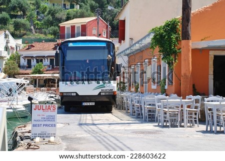 PAXOS, GREECE - JUNE 14, 2014: The local island bus negotiates the narrow seafront road at Loggos on the Greek island of Paxos. Taverna diners have to vacate their seats to allow the bus to pass.