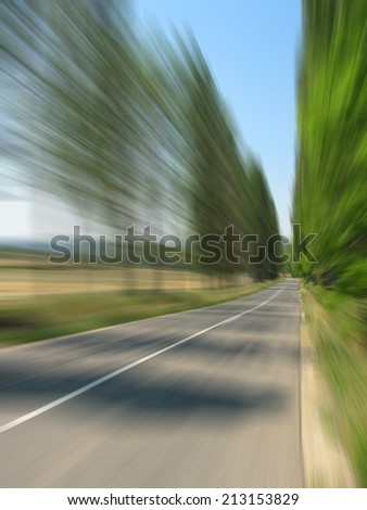 High speed road travelling - motion blurred image of summer road with bordering trees