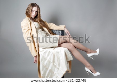 beautiful woman with long legs in a light coat and high-heels posing in the studio