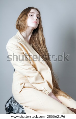 beautiful woman in a light coat and high-heels posing in the studio