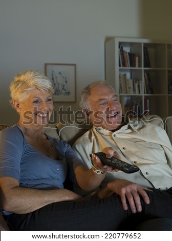 Evening scene of a happy elderly couple watching television in their living room