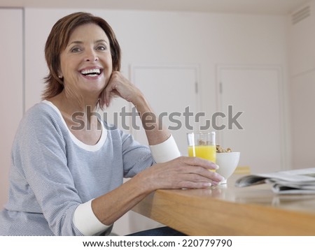 Relaxed portrait of woman at contemporary breakfast bar holding a glass of orange juice