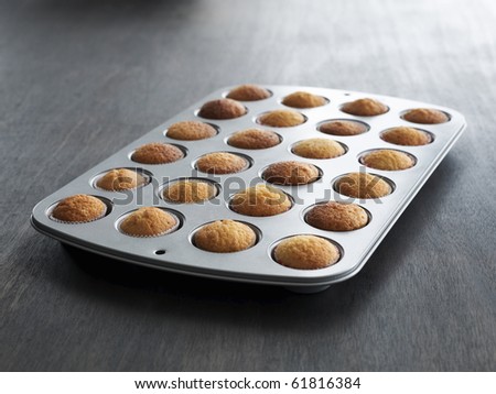 rows of freshly baked undecorated cupcakes on a dark table in a baking tray