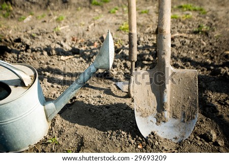 A watering can, a  spade and a small mattock on the ground in a peasant\'s kitchen garden
