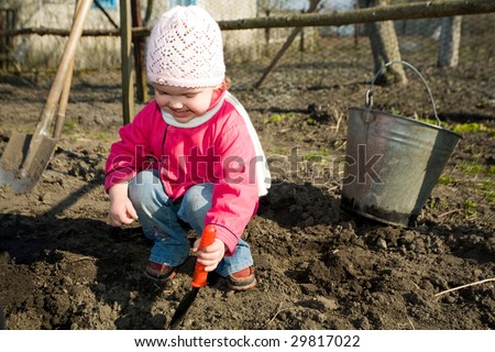 An  anxious little girl squatting down on the ground  cultivating soil  with  her  toy  spade