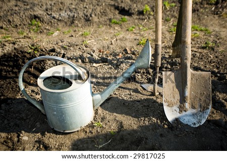 A watering can, a  spade and a  mattock on the ground in a peasant\'s kitchen garden