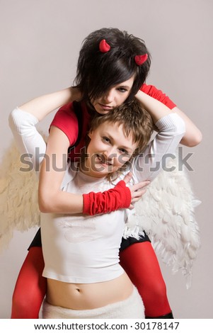 A smiling angel on her knees and a devil standing behind  the back and embracing her