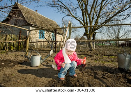 A pretty little girl squatting down on the ground cultivating soil with  a toy  spade