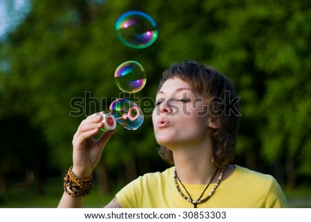 A young woman  blowing up soap-bubbles on the green tree background