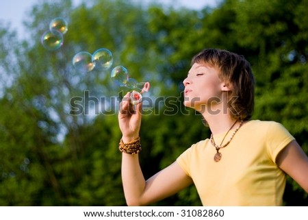 A young woman  blowing up soap-bubbles on the green trees background