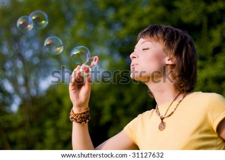 A young woman  blowing up soap-bubbles on the green trees background
