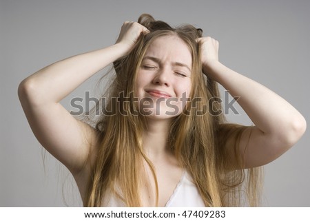Stress and frustrated woman with hands in her long hair pulling. On grey background.