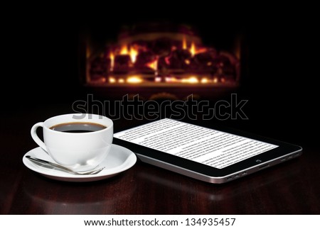 Cap of coffee and tablet on the table top with fireplace in the background.