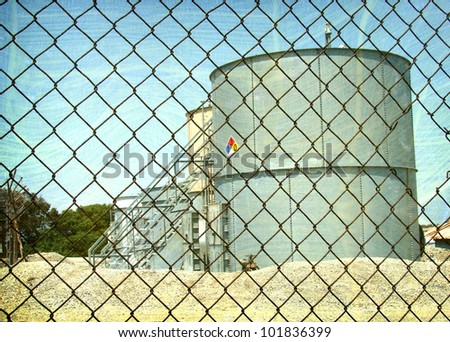 aged and worn vintage photo of  industrial oil tanks behind fence
