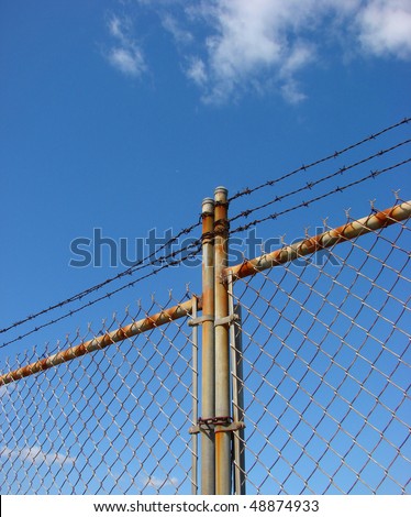 old rusted chain link fence and barbed wire with bright blue sky