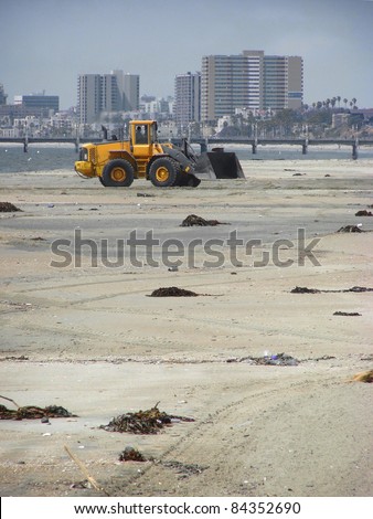 tractor moving sand on beach with city buildings in background